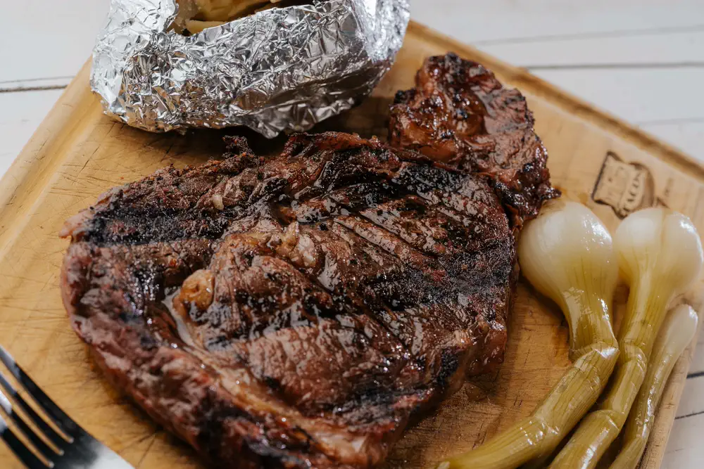 Corte a la parrilla con papa al horno y cebollitas, en tabla de madera